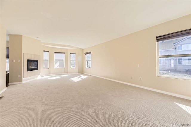 unfurnished living room with light carpet, a tiled fireplace, and baseboards