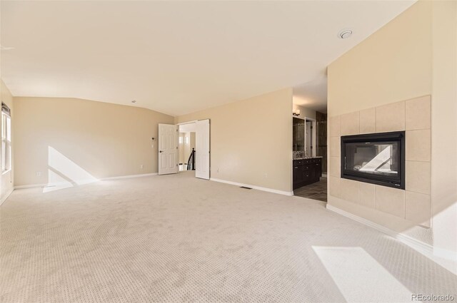 unfurnished living room with baseboards, vaulted ceiling, a tiled fireplace, and light colored carpet