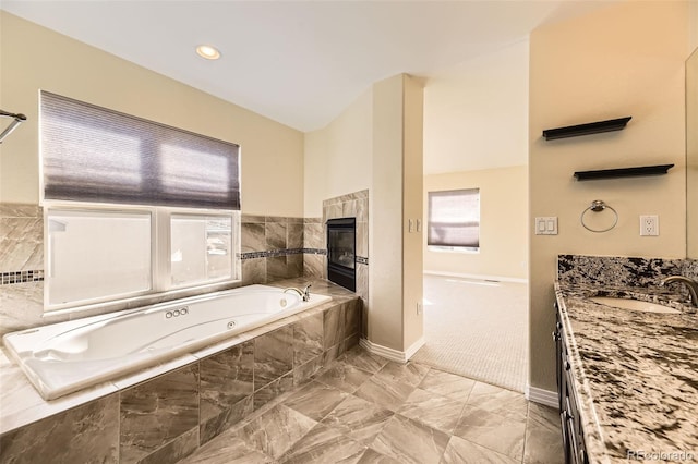 bathroom featuring a tile fireplace, baseboards, vanity, and a tub with jets