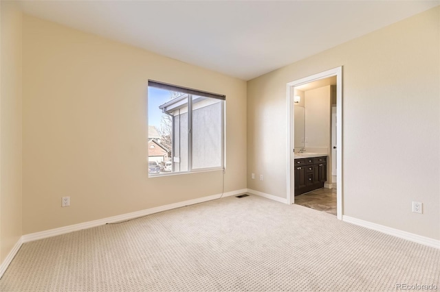 unfurnished bedroom featuring visible vents, baseboards, ensuite bath, carpet flooring, and a sink