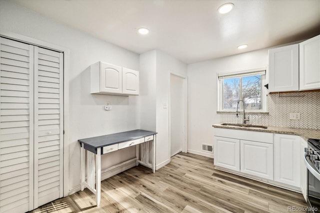 kitchen with stainless steel range oven, sink, tasteful backsplash, light hardwood / wood-style floors, and white cabinets