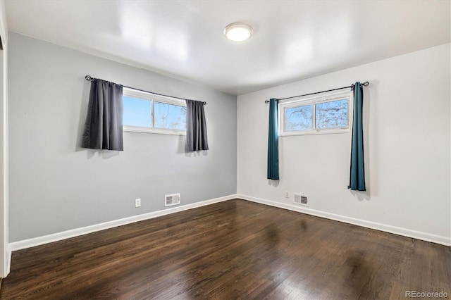 spare room with plenty of natural light, dark wood finished floors, and visible vents