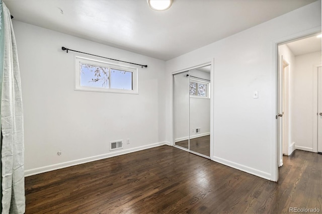 unfurnished bedroom with a closet, wood finished floors, visible vents, and baseboards