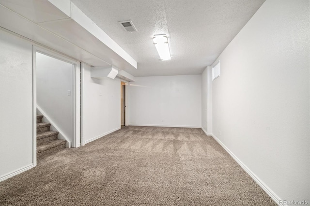 finished below grade area with carpet, visible vents, stairway, a textured ceiling, and baseboards