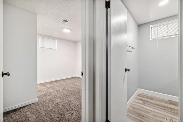 hallway with carpet floors, baseboards, visible vents, and a textured ceiling