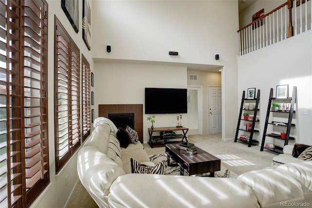 carpeted living room with a towering ceiling and a tiled fireplace