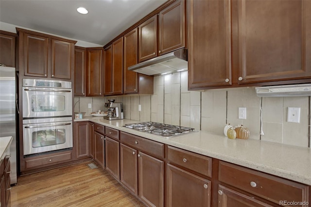 kitchen featuring appliances with stainless steel finishes, decorative backsplash, light stone countertops, and light wood-type flooring