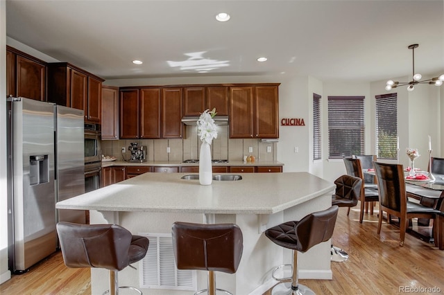 kitchen featuring decorative backsplash, a center island, a notable chandelier, light wood-type flooring, and appliances with stainless steel finishes