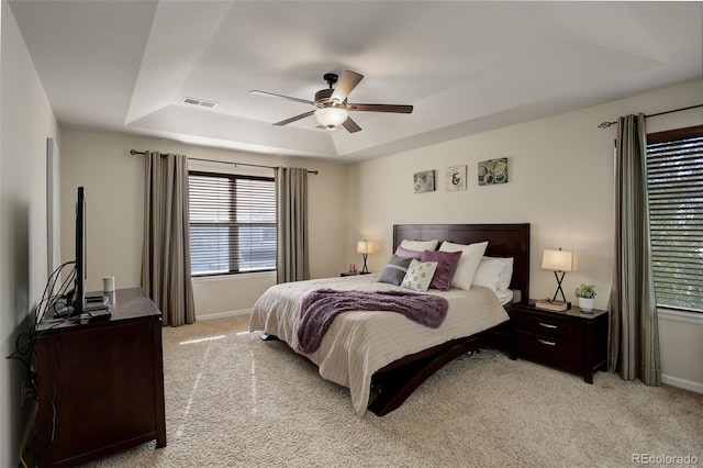 bedroom with light colored carpet, a raised ceiling, and ceiling fan