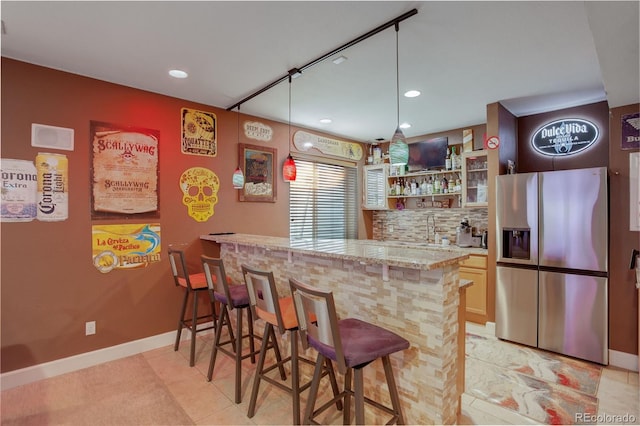 bar with decorative backsplash, sink, stainless steel fridge, light stone countertops, and light tile patterned flooring