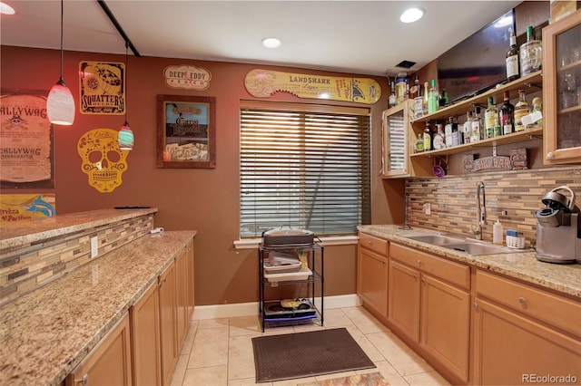 kitchen with tasteful backsplash, light stone countertops, sink, light tile patterned flooring, and decorative light fixtures