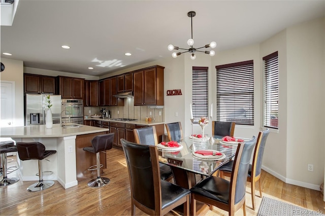 dining space with sink, light hardwood / wood-style flooring, and a chandelier