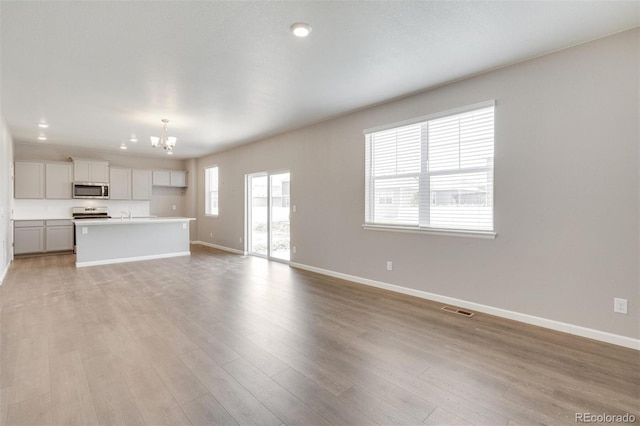 unfurnished living room with a chandelier and light hardwood / wood-style floors