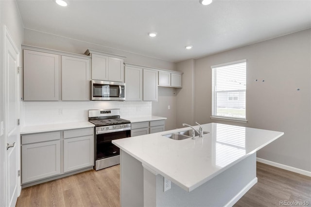 kitchen with sink, stainless steel appliances, backsplash, an island with sink, and light hardwood / wood-style floors