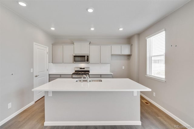 kitchen with white cabinetry, sink, a kitchen island with sink, appliances with stainless steel finishes, and light wood-type flooring