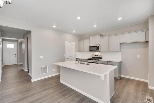 kitchen with appliances with stainless steel finishes, a kitchen island with sink, sink, gray cabinets, and light hardwood / wood-style floors