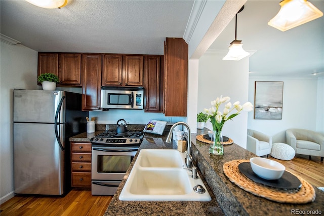 kitchen featuring stainless steel appliances, decorative light fixtures, light hardwood / wood-style floors, sink, and crown molding