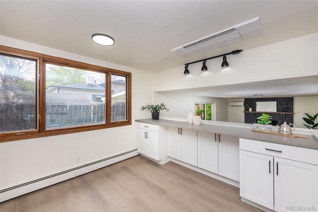 kitchen with baseboard heating, light hardwood / wood-style flooring, white cabinetry, brick wall, and track lighting