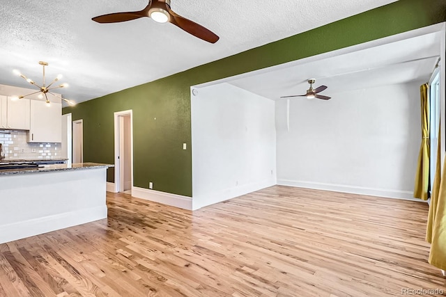 unfurnished living room with a textured ceiling, ceiling fan with notable chandelier, baseboards, and light wood-style floors