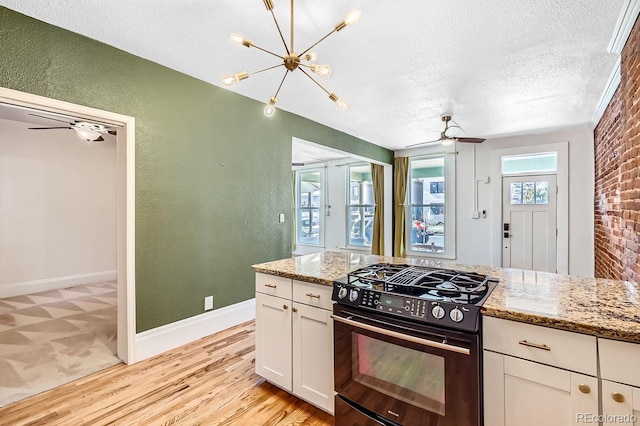 kitchen with white cabinets, range with gas stovetop, a textured wall, light stone counters, and a textured ceiling