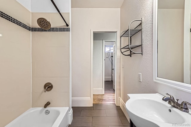 full bath featuring a textured wall, a sink, shower / bathing tub combination, and baseboards