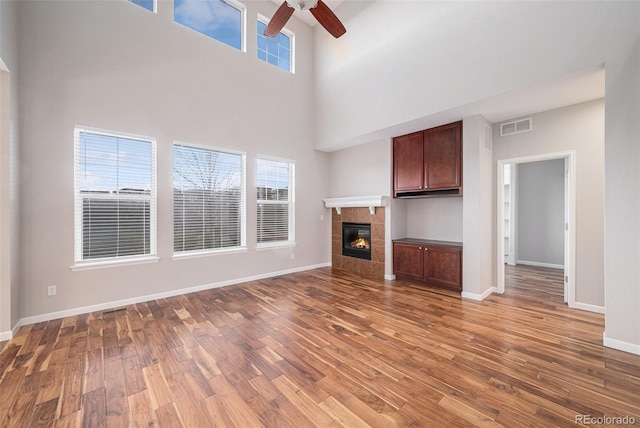 unfurnished living room featuring ceiling fan, visible vents, wood finished floors, and a towering ceiling