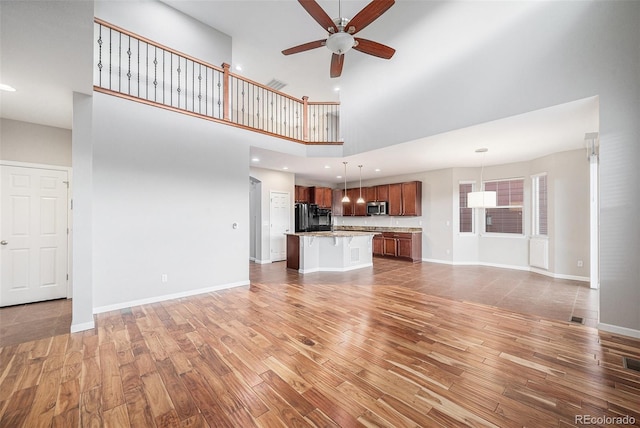 unfurnished living room featuring baseboards, ceiling fan, light wood-type flooring, and a towering ceiling