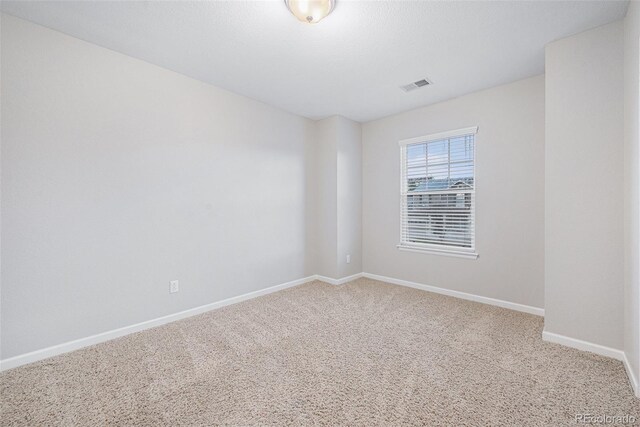 carpeted spare room featuring baseboards and visible vents