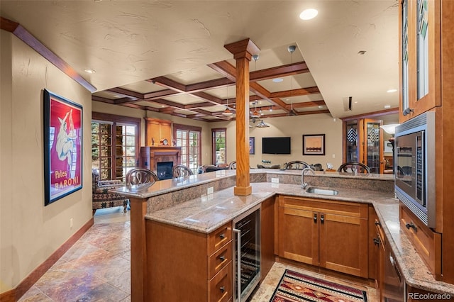 kitchen featuring sink, light stone counters, stainless steel microwave, kitchen peninsula, and beverage cooler