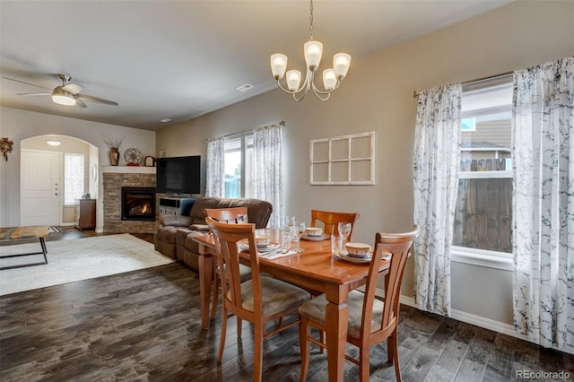 dining room featuring plenty of natural light, dark wood-type flooring, ceiling fan with notable chandelier, and a fireplace