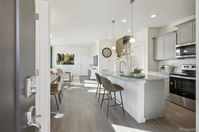 kitchen featuring tasteful backsplash, appliances with stainless steel finishes, wood finished floors, gray cabinets, and a kitchen bar