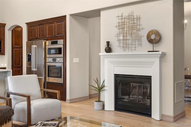 15252 W Warren Dr, Lakewood, CO 80228 - living area featuring visible vents, a glass covered fireplace, light wood-style floors, baseboards, and arched walkways