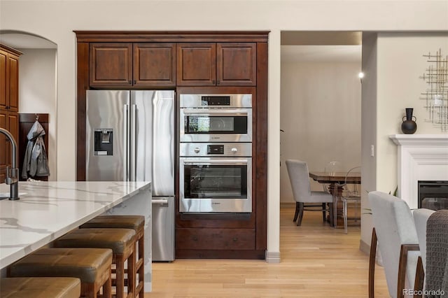 15252 W Warren Dr, Lakewood, CO 80228 - kitchen with light wood-style floors, light stone countertops, stainless steel appliances, and a kitchen bar