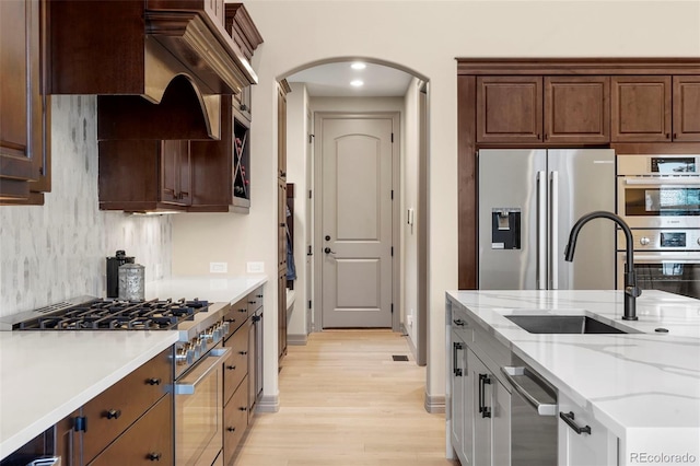 15252 W Warren Dr, Lakewood, CO 80228 - kitchen with a sink, light stone counters, arched walkways, light wood finished floors, and appliances with stainless steel finishes