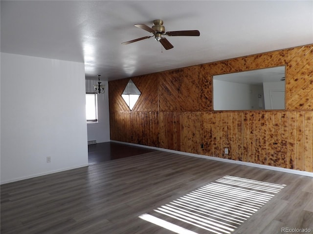 empty room featuring ceiling fan with notable chandelier, dark wood-type flooring, and wood walls