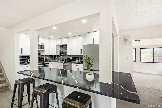 206 Troy St, Aurora, CO 80011 - kitchen featuring appliances with stainless steel finishes, backsplash, a breakfast bar area, white cabinets, and recessed lighting