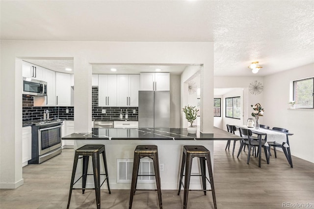206 Troy St, Aurora, CO 80011 - kitchen featuring appliances with stainless steel finishes, a breakfast bar, light wood-style flooring, backsplash, and a textured ceiling