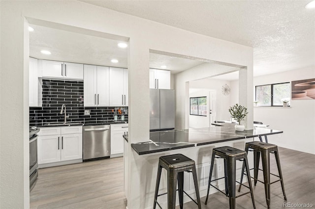 206 Troy St, Aurora, CO 80011 - kitchen with stainless steel appliances, dark countertops, a breakfast bar area, light wood-type flooring, and a textured ceiling