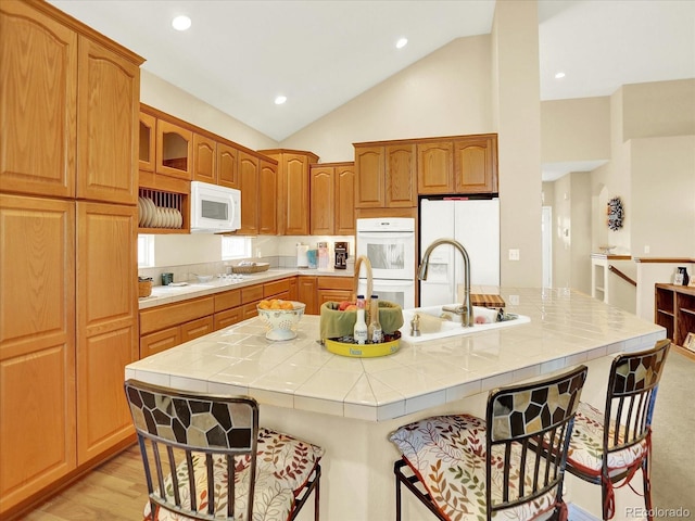 11556 W Cooper Pl, Littleton, CO 80127 - kitchen with white appliances, tile countertops, a kitchen bar, a large island with sink, and vaulted ceiling