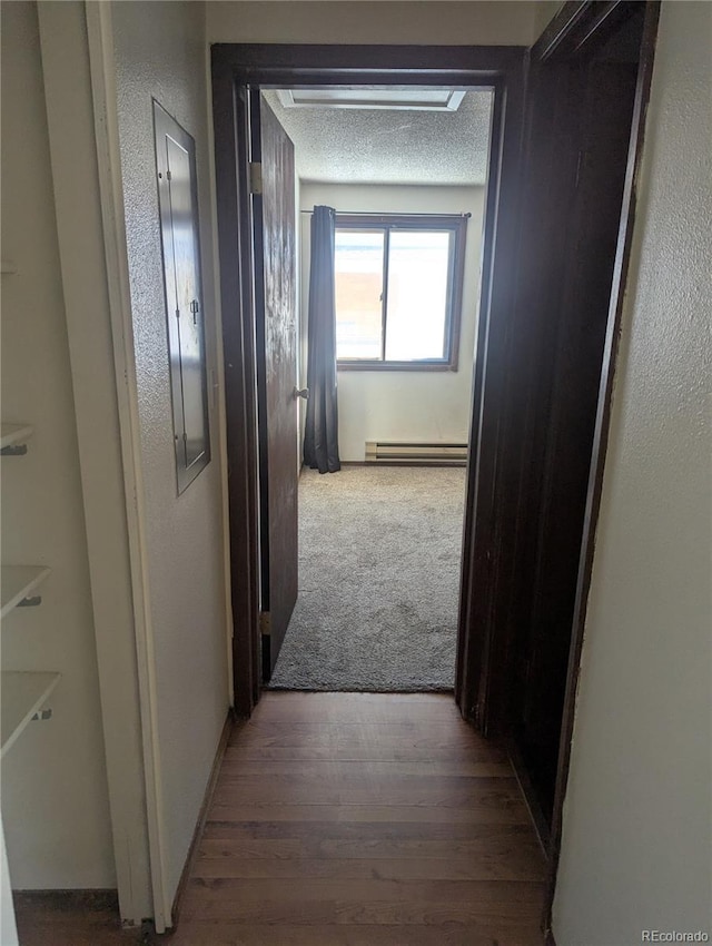 hall featuring a textured wall, a textured ceiling, baseboard heating, and wood finished floors