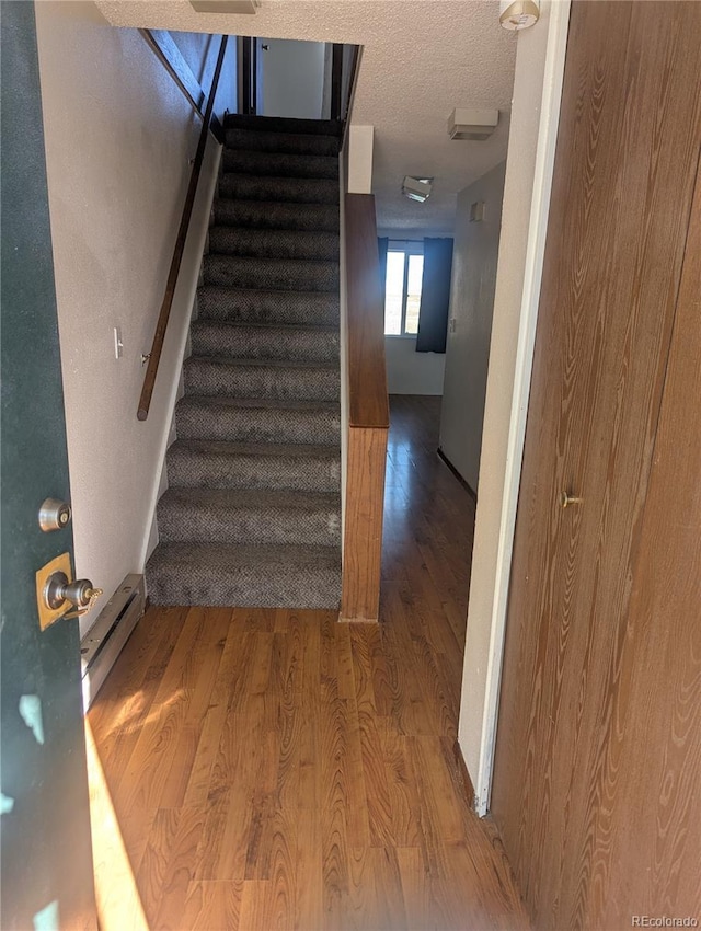 stairway with a baseboard radiator, a textured ceiling, and wood finished floors