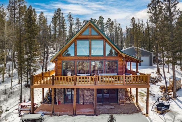 snow covered property with stone siding, an outdoor structure, and a wooden deck