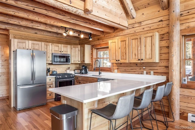 kitchen with wooden walls, a peninsula, stainless steel appliances, light countertops, and a sink