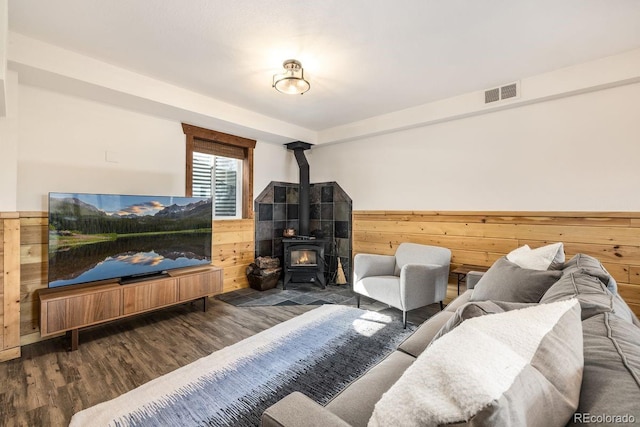 living room featuring wood walls, wood finished floors, visible vents, wainscoting, and a wood stove