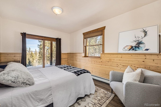 bedroom featuring a wainscoted wall, a baseboard heating unit, wood finished floors, and wooden walls