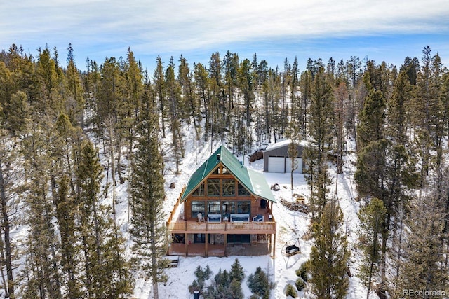 snow covered house featuring an outdoor structure and a forest view