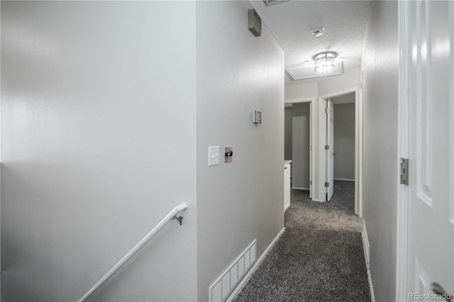 hall with dark carpet and a textured ceiling