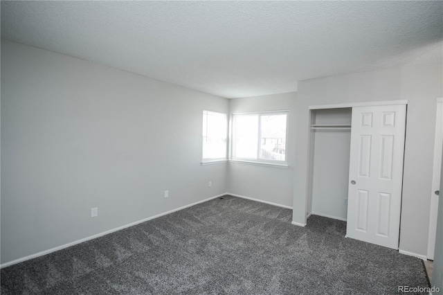 unfurnished bedroom with dark carpet, a textured ceiling, and a closet