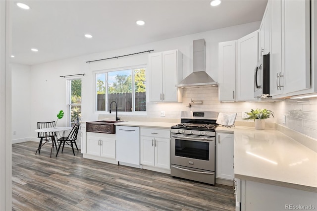 kitchen featuring white cabinets, appliances with stainless steel finishes, wall chimney exhaust hood, sink, and backsplash