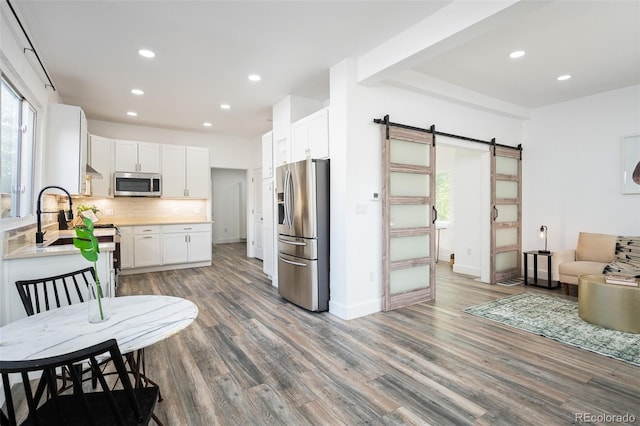 kitchen featuring white cabinets, a barn door, a healthy amount of sunlight, and stainless steel appliances